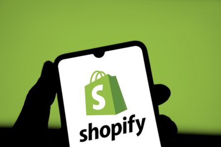 A silhouette of a hand holding a phone with a shopify logo on the screen