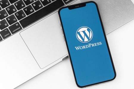 A phone sitting on a desk, leaning against a laptop, with the WordPress logo on the screen